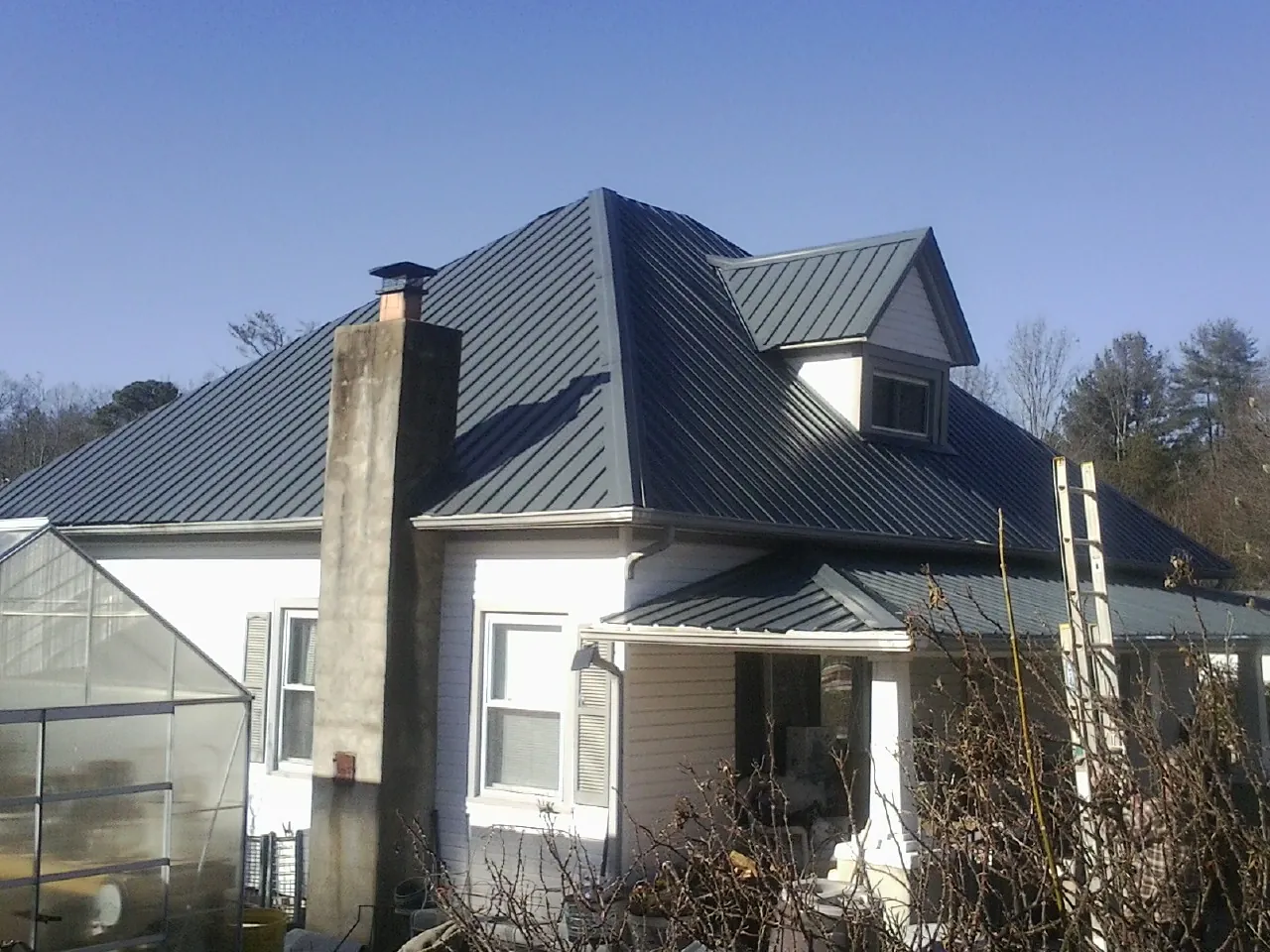 Dark blue standing seam metal roof on a white farmhouse with dormer — Slate & Tile Roof Repair by Roofing Brothers in Amboy