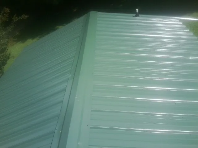 New green metal panels meeting at the ridge of a roof — Flat Roof Repair work by our crew in Amboy