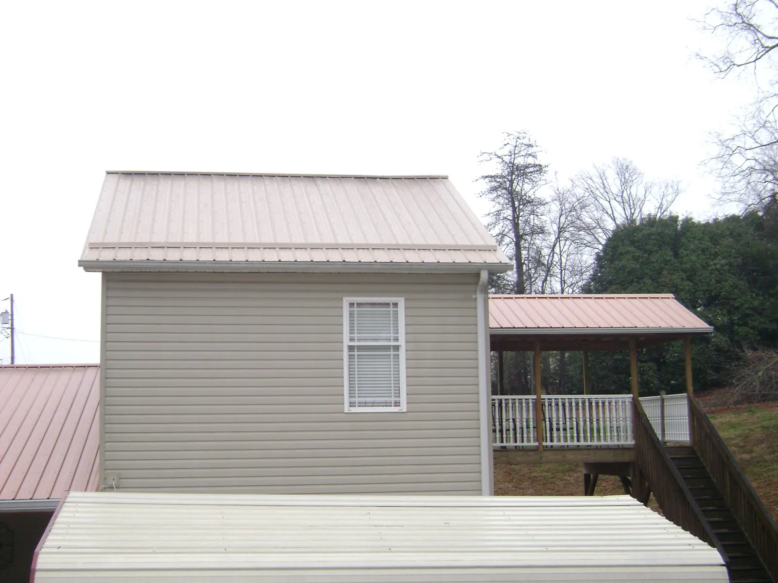 Tan metal roofs on a two story addition and attached porch, from a Roof Replacement job in Amboy